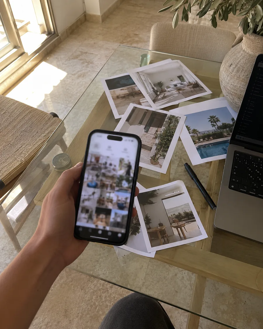 Un móvil muestra la cuadrícula de un perfil inmobiliario junto a fotografías impresas sobre la mesa